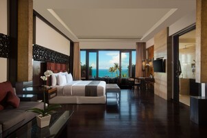 Quarto de hotel moderno com uma cama grande, sofá, escrivaninha e vista para o oceano.