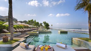 A poolside area with lounge chairs, a table with drinks, and a view of the ocean.
