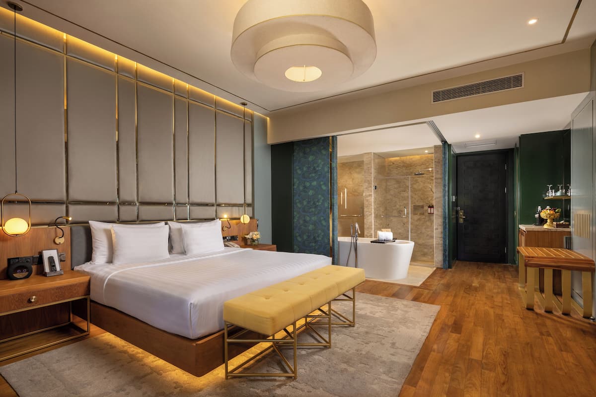A modern hotel room with a large bed, bedside tables, a bench, a bathroom with a bathtub, and a shower.