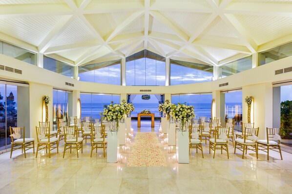 A spacious hall with a high ceiling and large windows, arranged in rows of chairs facing a central aisle.