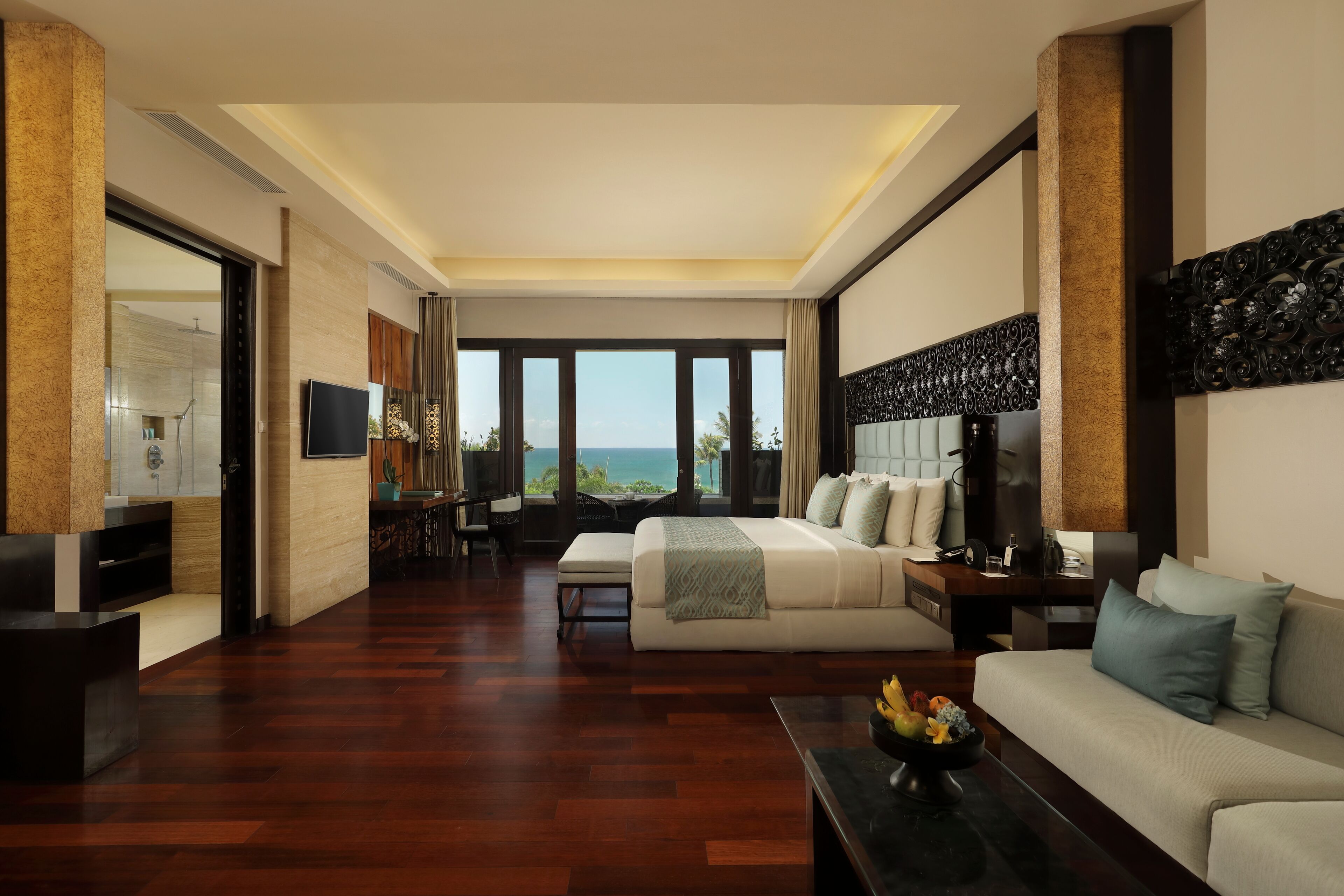 Habitación de hotel moderna con una cama grande, un sofá, un televisor y vista al océano.