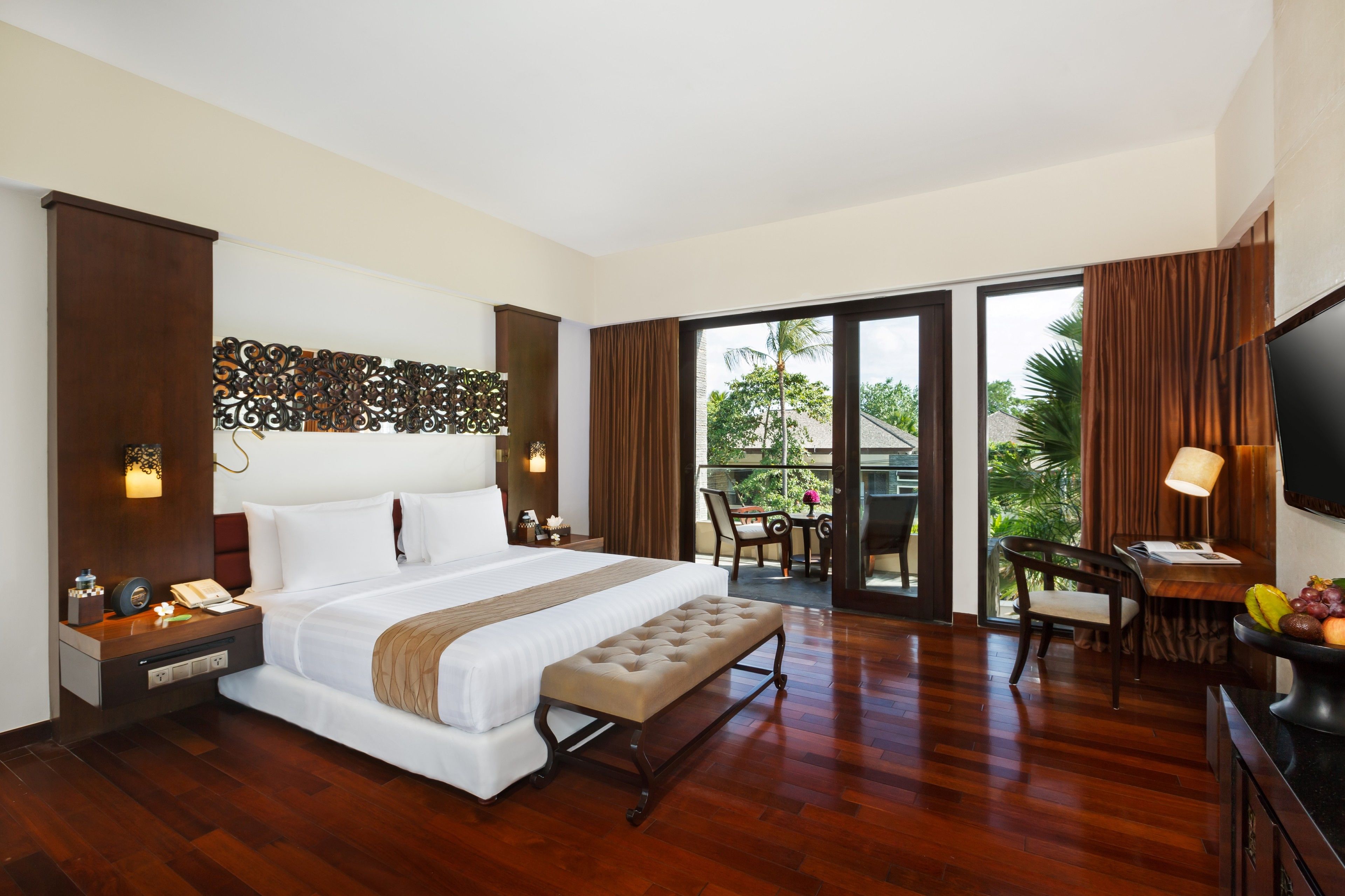 Une chambre d’hôtel avec un grand lit, un bureau avec une chaise, une télévision et un balcon équipé d’une table et de chaises.