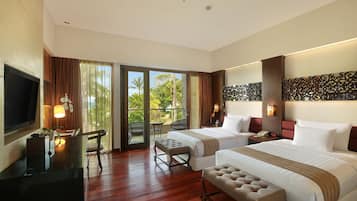 A hotel room with two beds, a TV, a desk, and a balcony with a view of greenery.