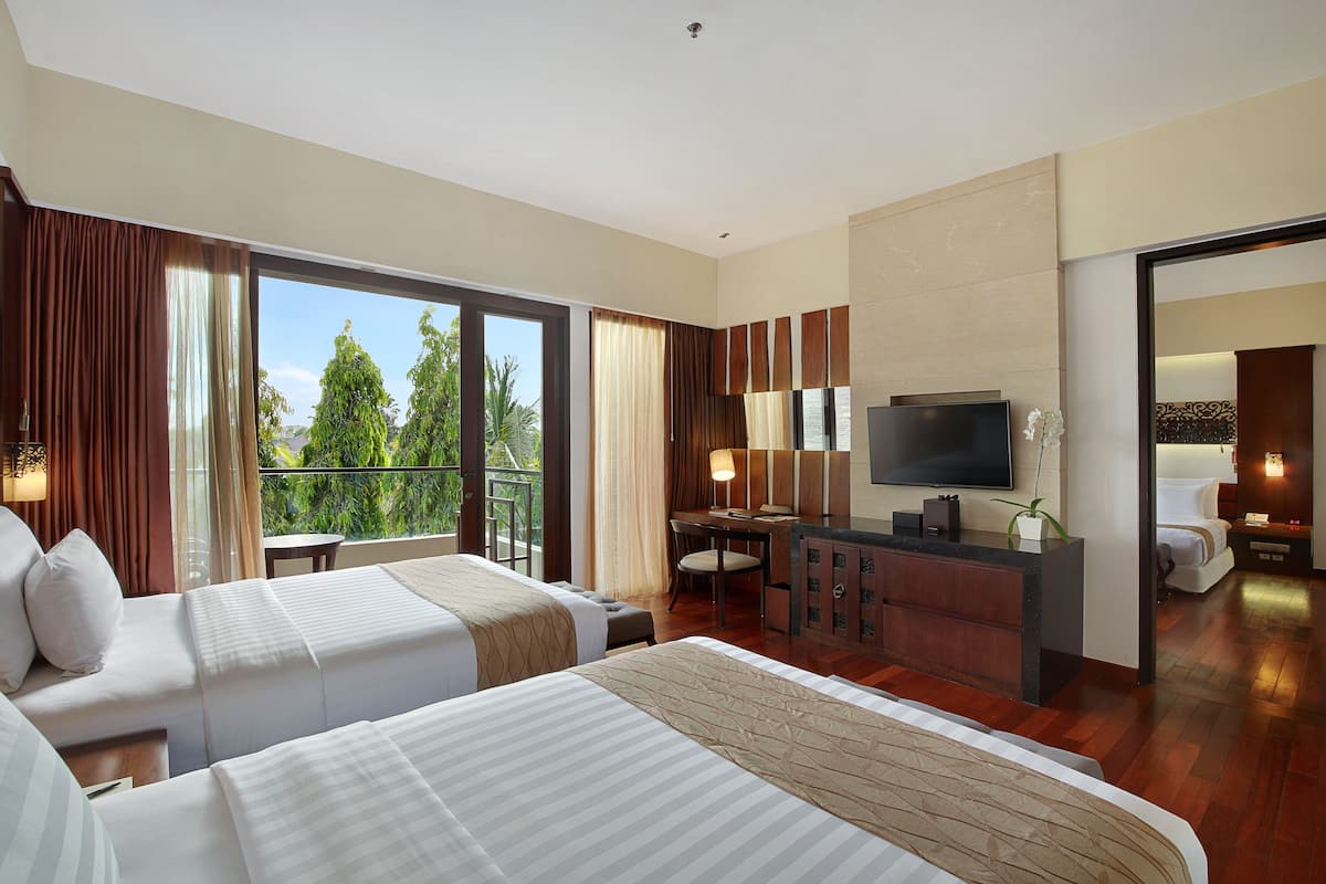 A hotel room with two beds, a desk, a TV, and a balcony with a view of trees.