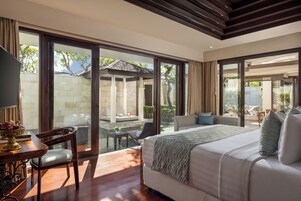 Um quarto espaçoso com uma cama grande, um espaço de estar com sofá e cadeiras, e vista para uma piscina e jardim através de grandes portas de vidro deslizantes.