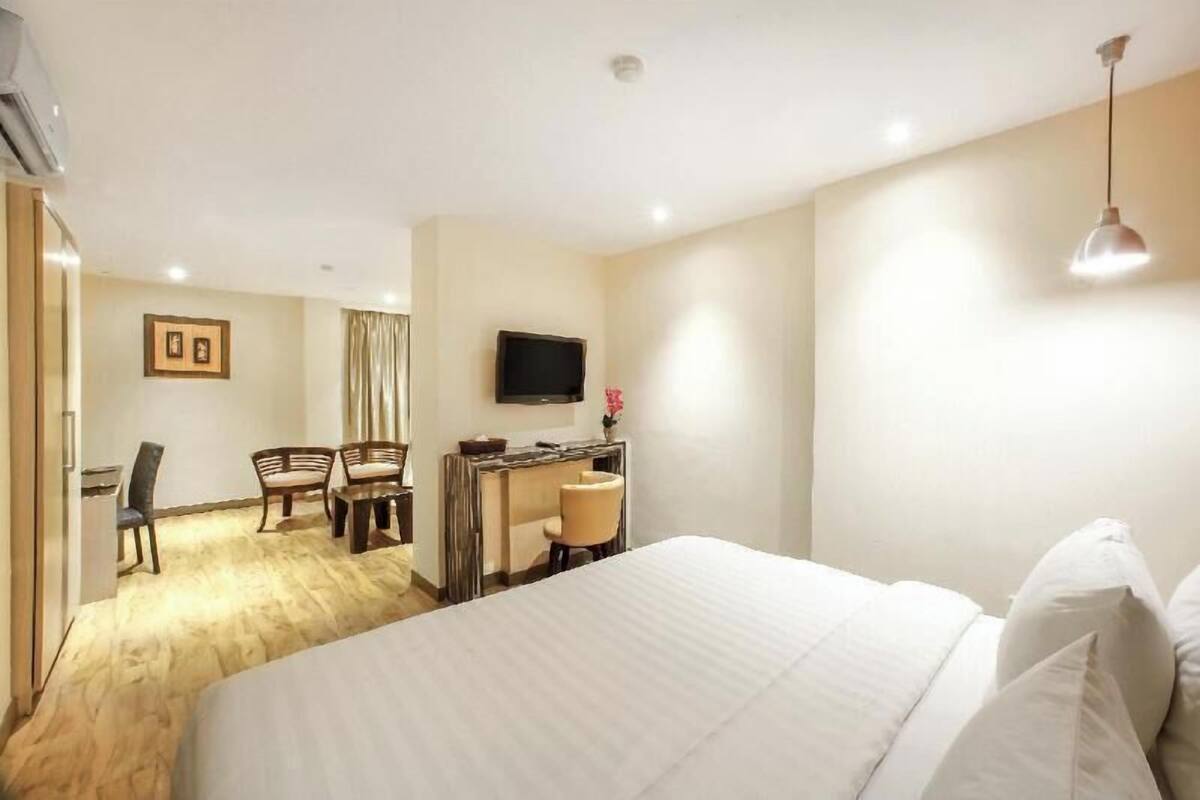 A hotel room with a bed, a desk, two chairs, a television, and a window.