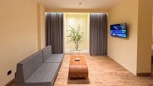 A modern living room with a grey sofa, a wooden coffee table, and a TV mounted on the wall. - The Rivavi Legian (Legian)