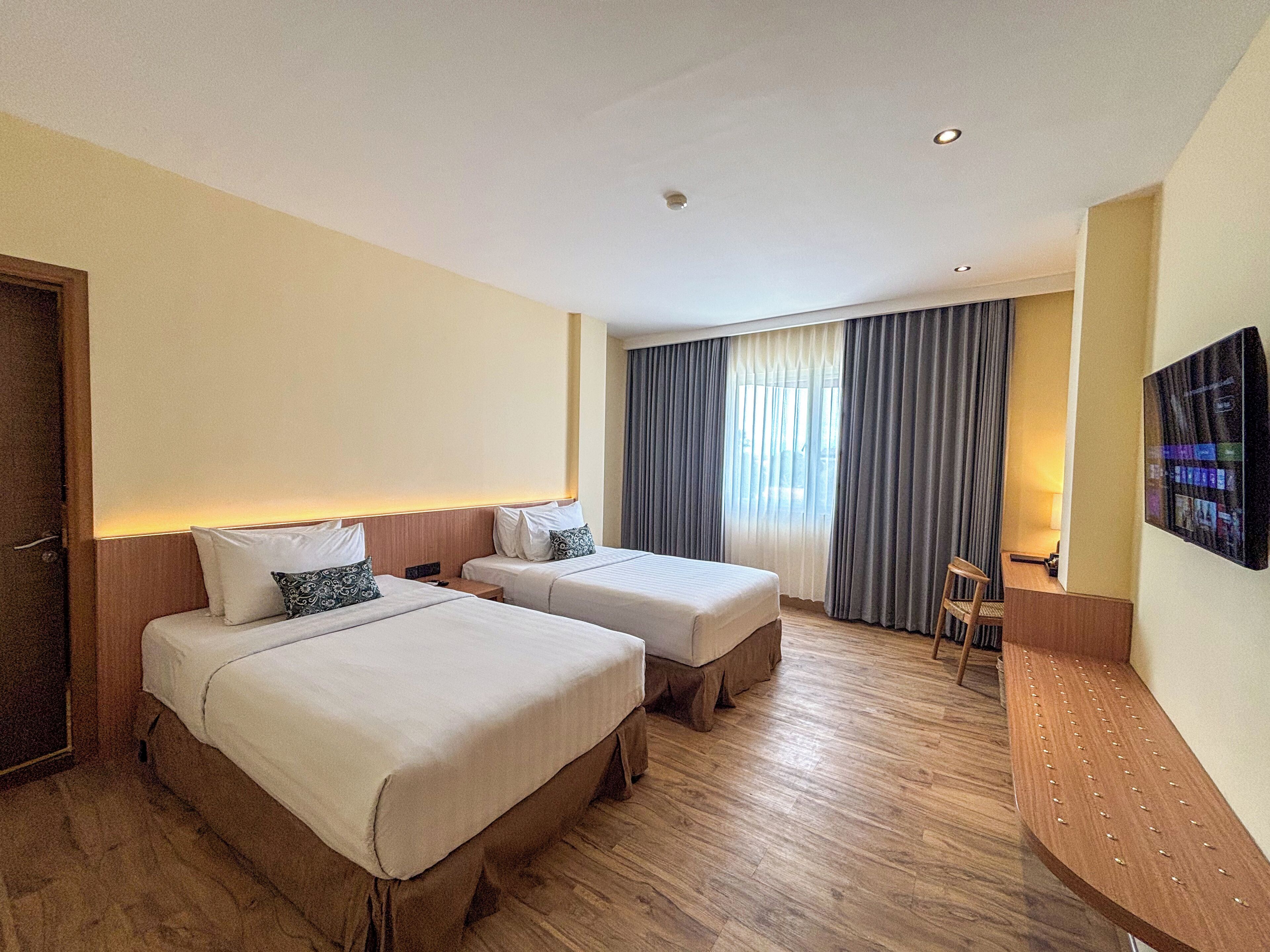 A hotel room with two beds, a desk, a chair, and a TV mounted on the wall.