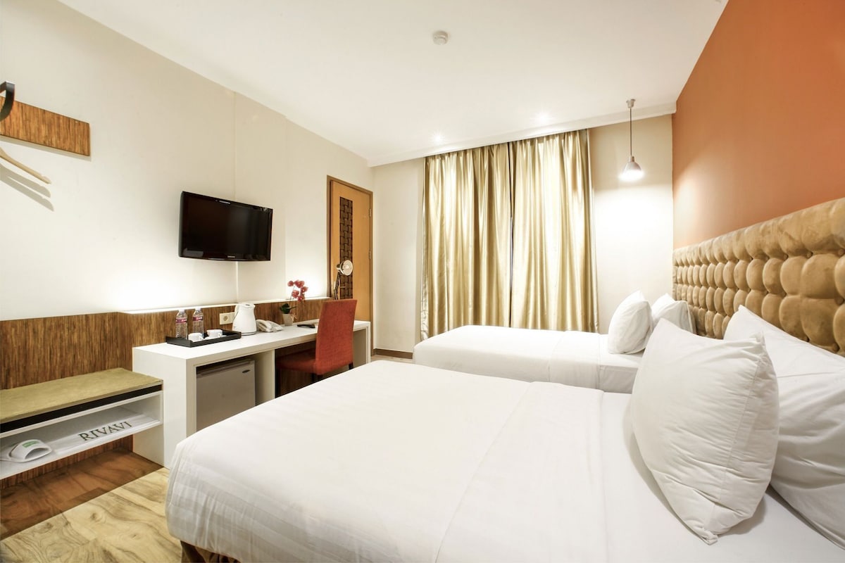 A hotel room with a bed, a desk, a television, and a window with curtains.