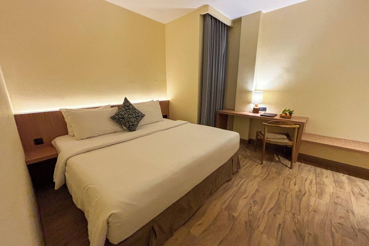 A hotel room with a large bed, a desk, and a chair.