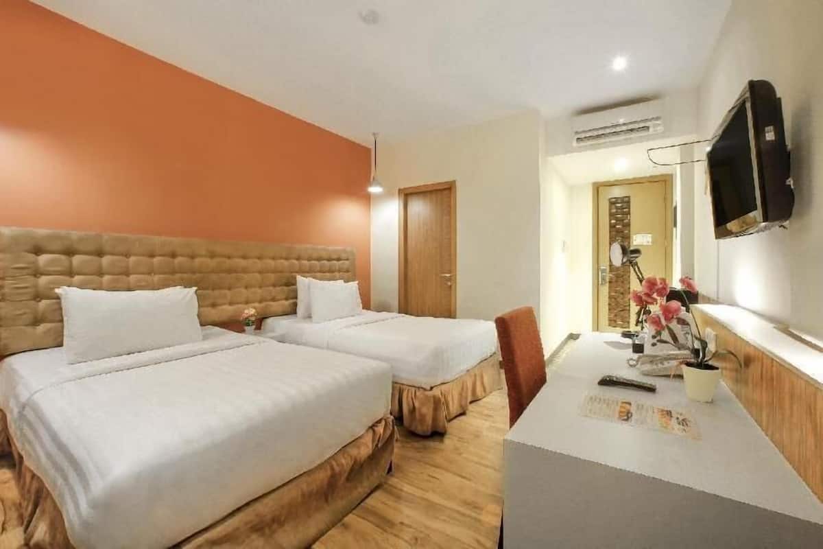 A hotel room with two beds, a desk, a television, and a door.