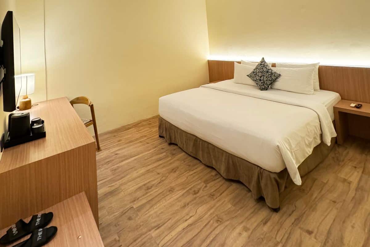 A hotel room with a bed, bedside table, lamp, and a desk with a chair.