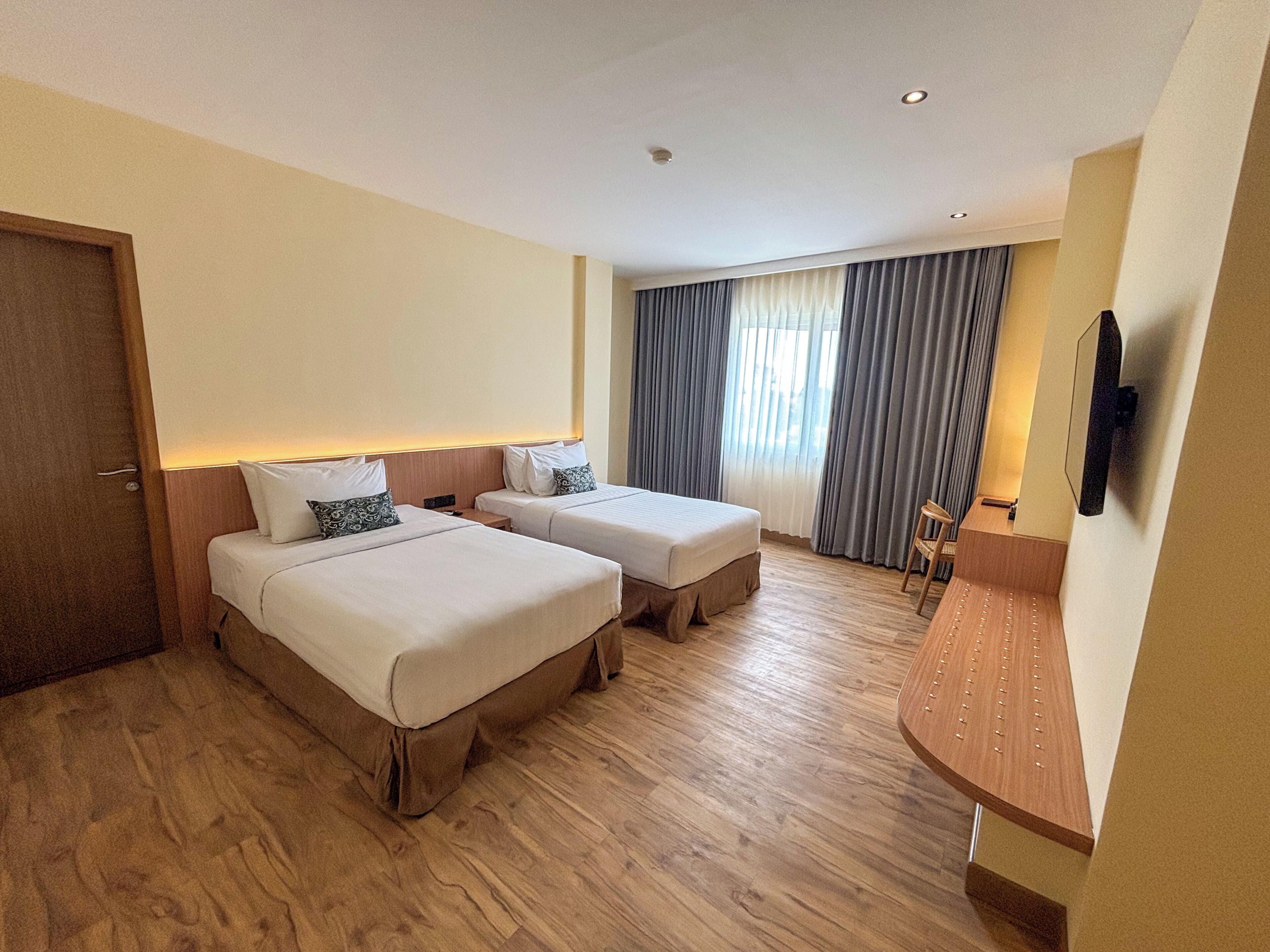 Habitación de hotel con dos camas, suelo de madera, escritorio y televisor montado en la pared.