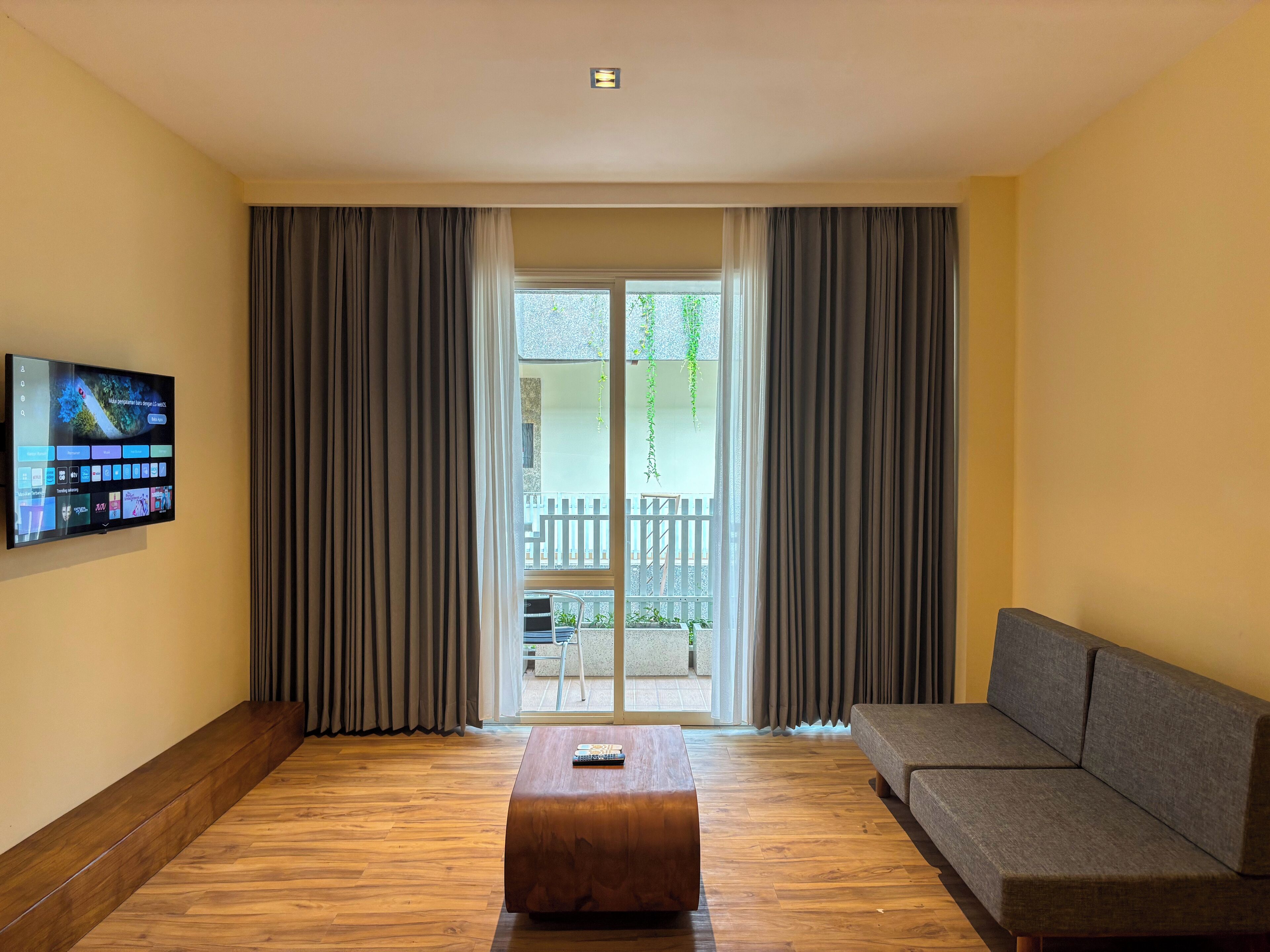 Una sala de estar moderna con suelo de madera, un sofá gris, una mesa de centro de madera y un televisor de pantalla plana montado en la pared.