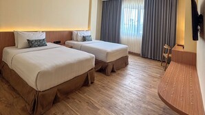 A hotel room with two beds, a wooden floor, a desk, and a large window with curtains. - The Rivavi Legian (Legian)