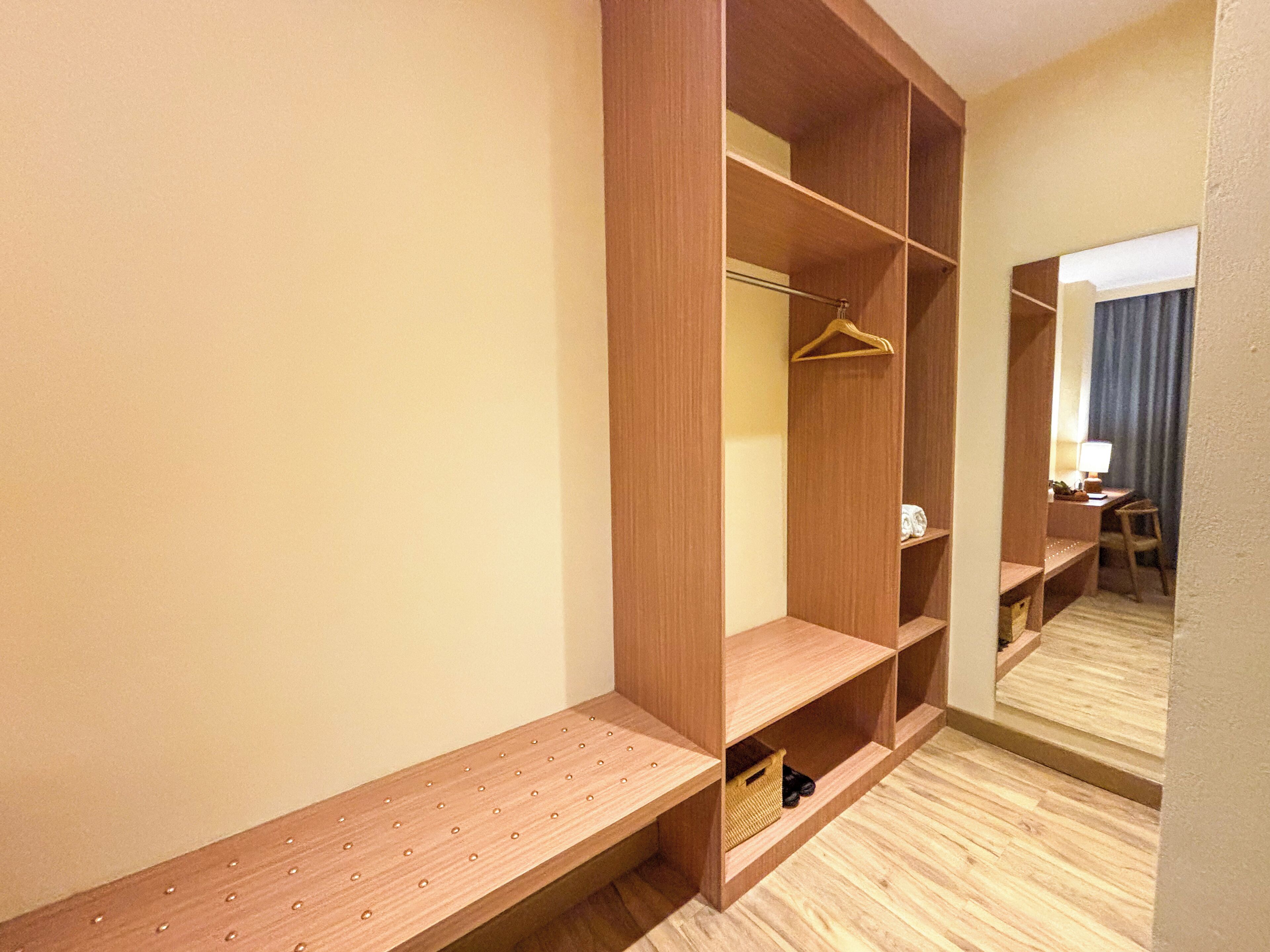 A walk-in closet with multiple shelves and hanging space, a bench, and a mirror.