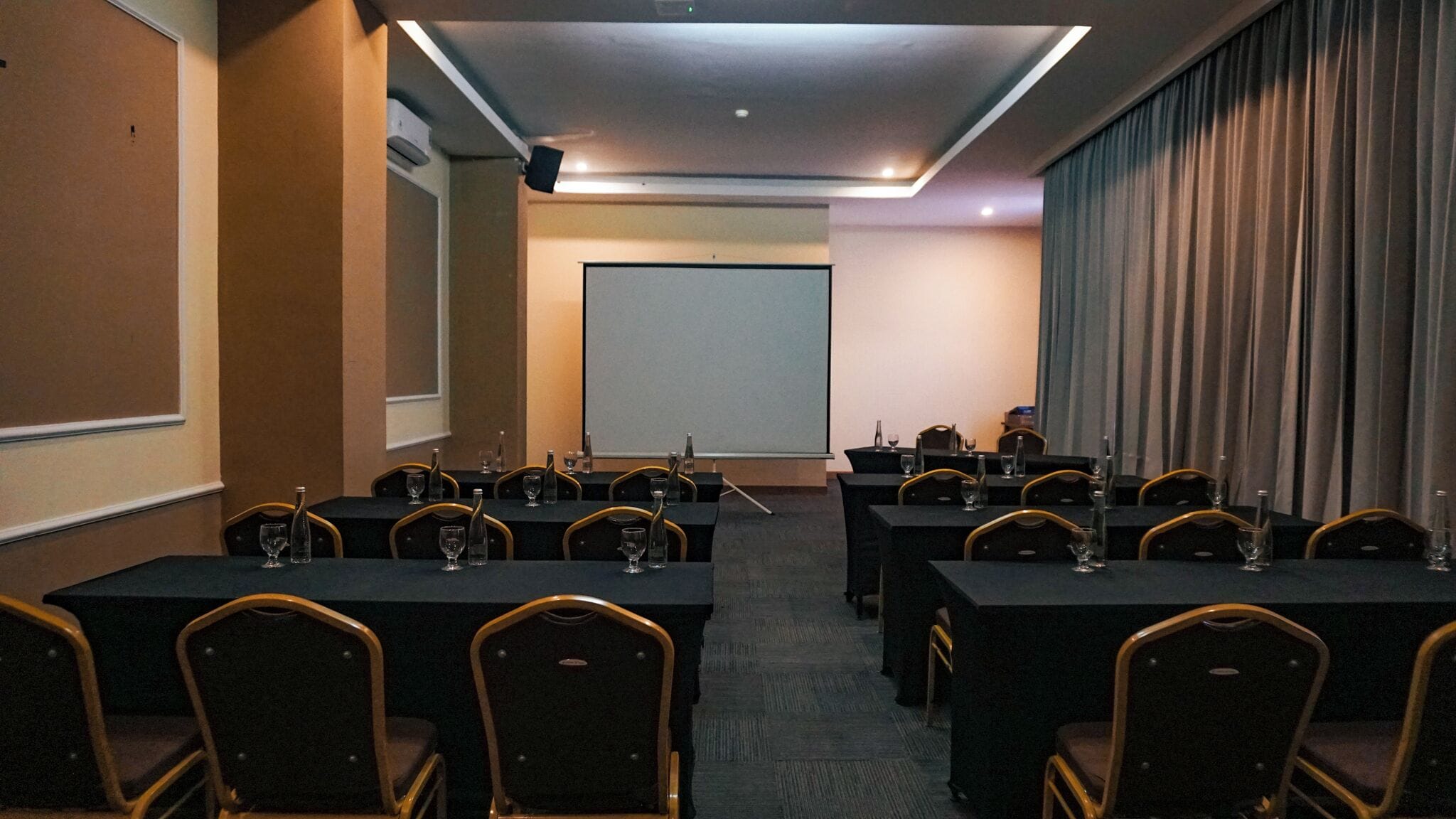 A conference room with tables and chairs, a projector screen, and a large window with curtains.