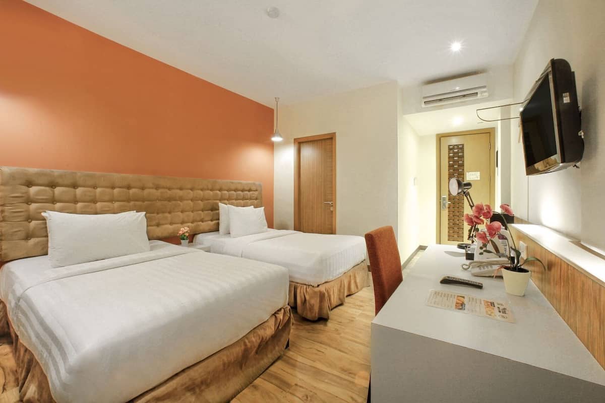 A hotel room with two beds, a desk, a chair, a TV, and an air conditioning unit.