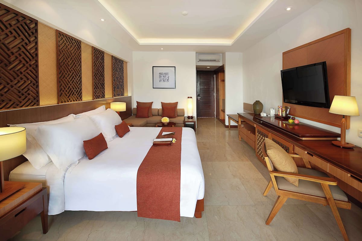 A hotel room with a large bed, a desk with a TV, and a chair.