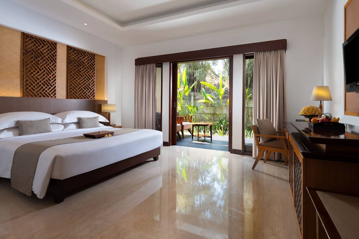 A hotel room with a large bed, a desk with a lamp, and a view of the outdoors through a sliding door.