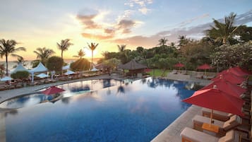 A pool area with lounge chairs and umbrellas, surrounded by palm trees and a view of the sunset.