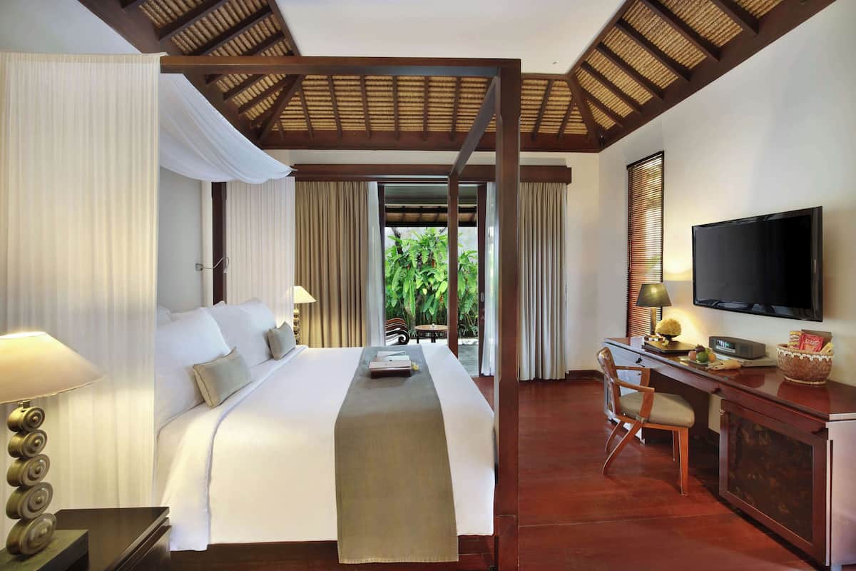A hotel room with a bed, a desk, a television, and a view of greenery outside.