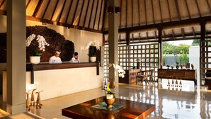 A reception area with a wooden reception desk, a seating area with chairs, and a decorative wall with plants and a large white orchid. - Bali Niksoma Boutique Beach Resort (Legian)