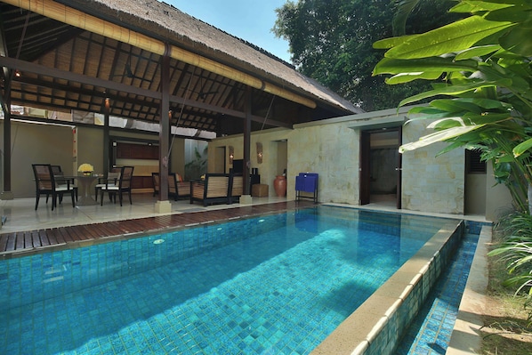 Piscina con borde de azulejos, rodeada por un porche cubierto con sillas y una mesa.