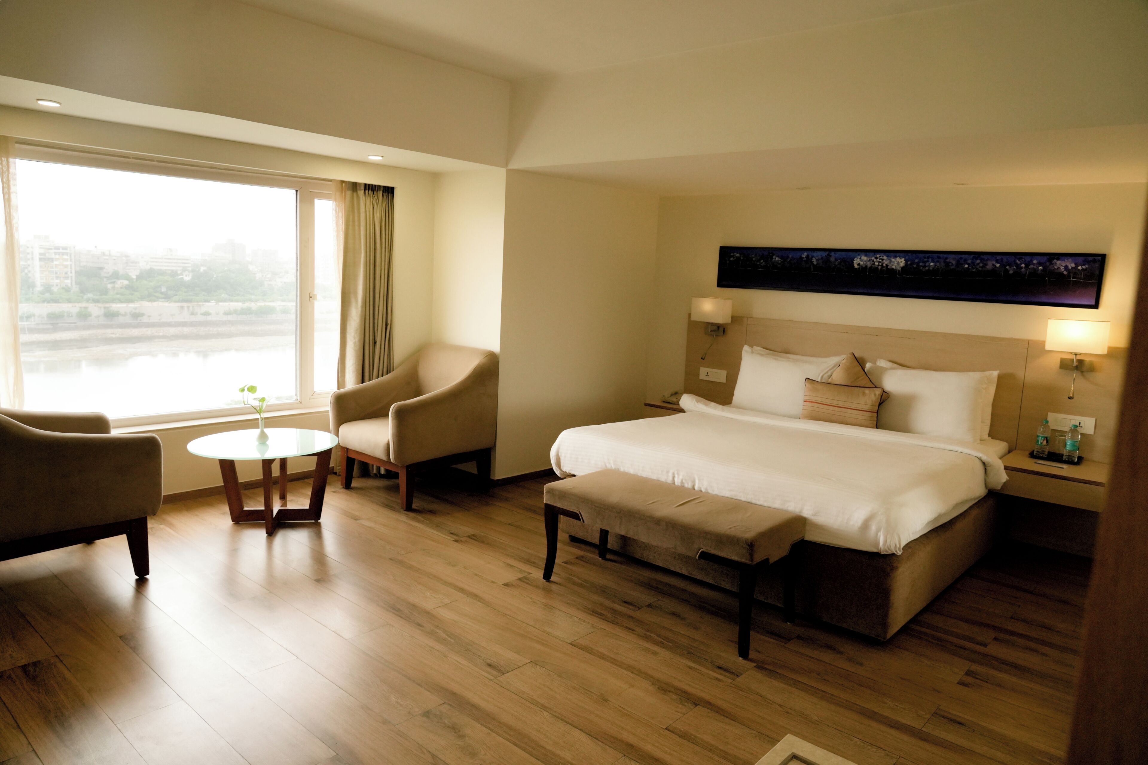 A hotel room with a bed, two armchairs, a small table, and a view of a river.