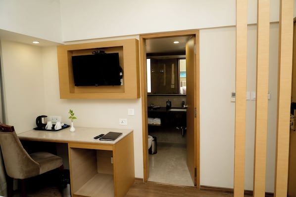 A hotel room with a desk, a chair, a television mounted on the wall, and a small plant on the desk.