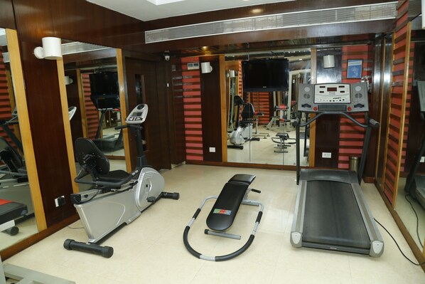 Ginásio com equipamentos de exercício, incluindo esteiras, bicicletas ergométricas e um remo.