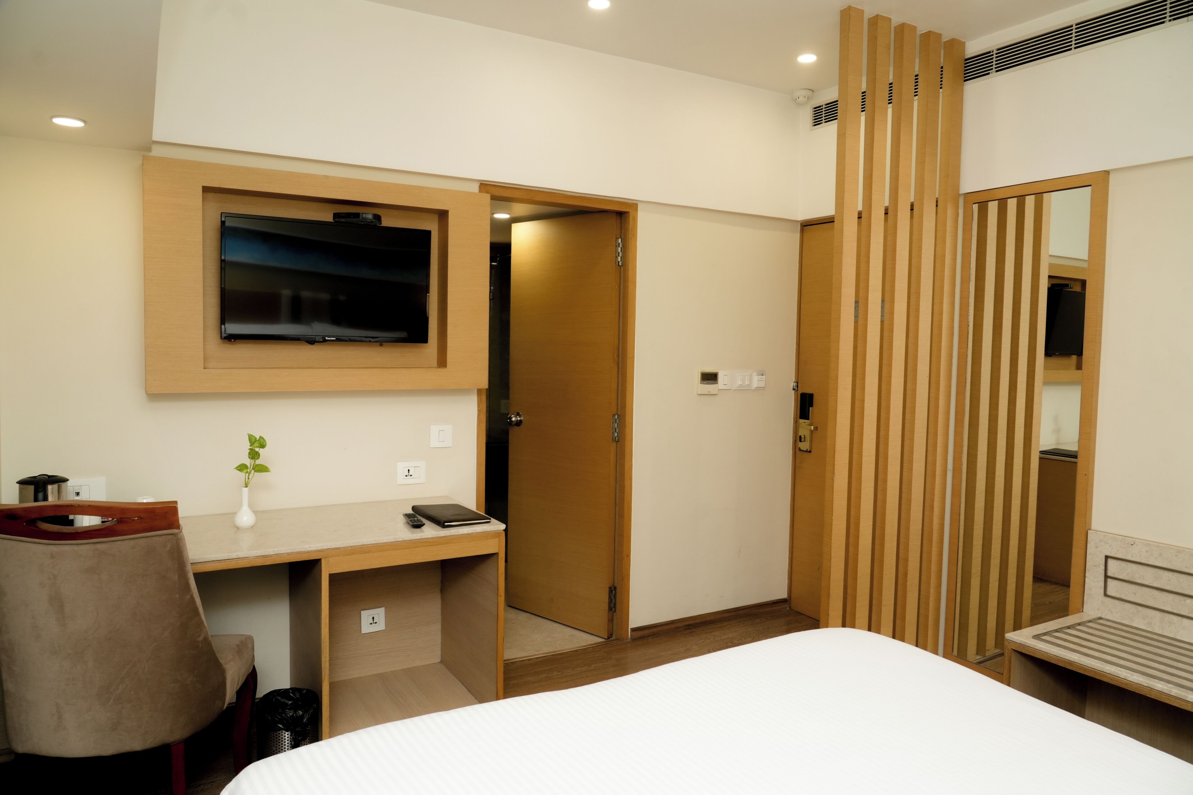 A hotel room with a bed, a desk with a chair, a TV mounted on the wall, and a sliding door.