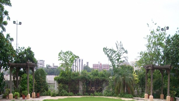 A well-maintained lawn with two wooden gazebos and a variety of trees and shrubs. - Rivera Sarovar Portico Ahmedabad (Ahmedabad)
