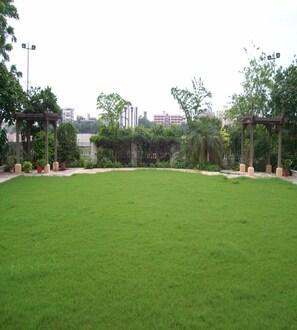 A well-maintained lawn with two wooden gazebos and a variety of trees and shrubs. - Rivera Sarovar Portico Ahmedabad (Ahmedabad)