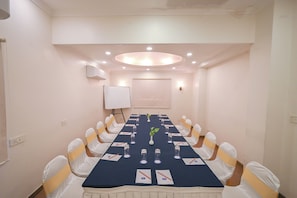 A conference room with a long table, white chairs, and a whiteboard. - Rivera Sarovar Portico Ahmedabad (Ahmedabad)