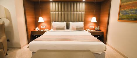 A hotel room with a large bed, two bedside tables, a chair, a bench, and a painting on the wall.