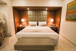 Una habitación de hotel con una cama grande, dos mesitas de noche, una silla, un banco y un cuadro en la pared.