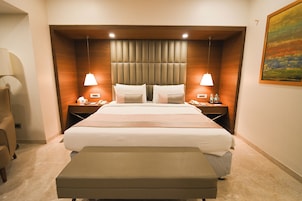 A hotel room with a large bed, two bedside tables, a chair, a bench, and a painting on the wall.
