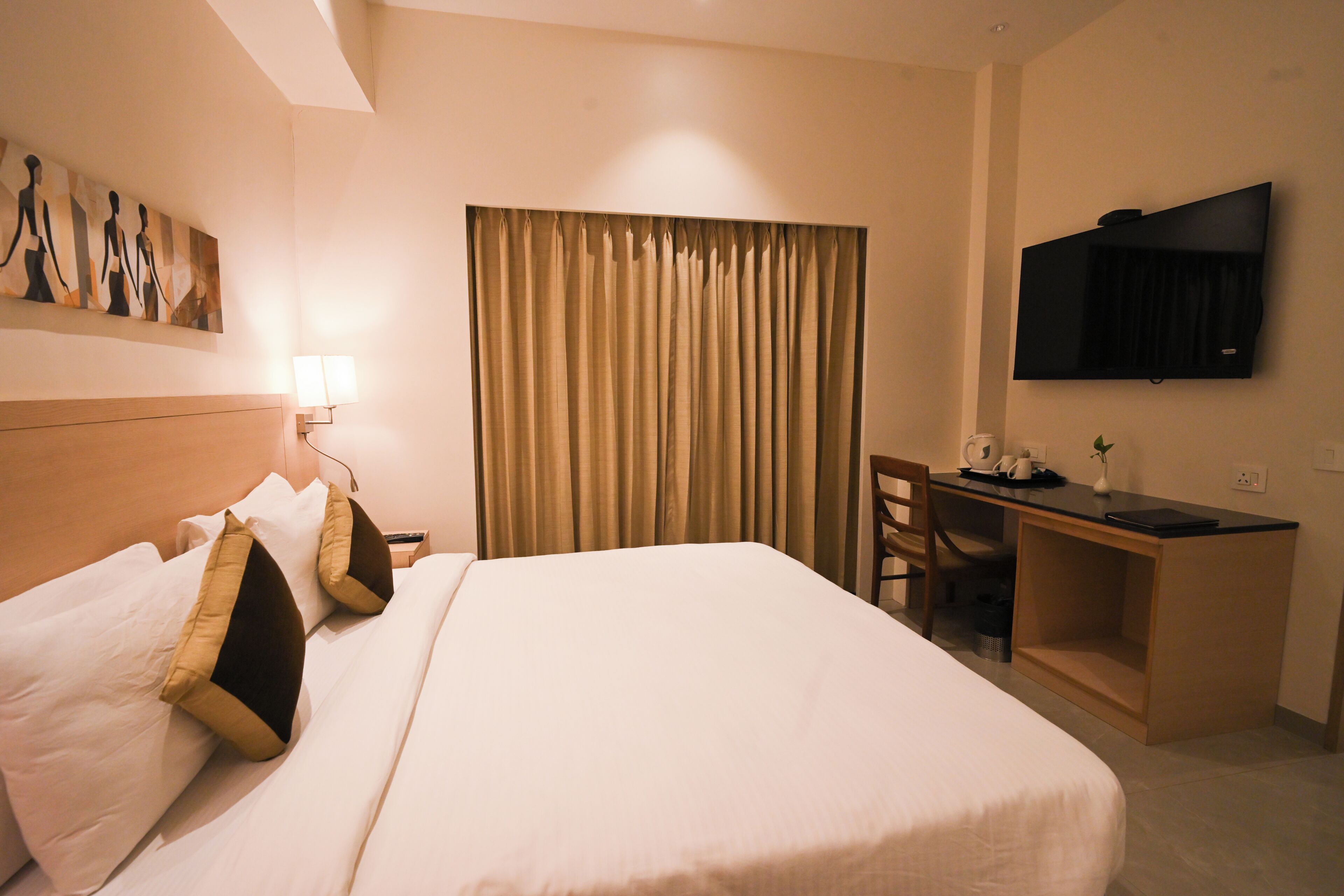 A hotel room with a bed, a desk, a chair, a television, and a painting on the wall.