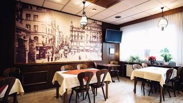 A restaurant with tables and chairs, a large mural on the wall, and a television screen.