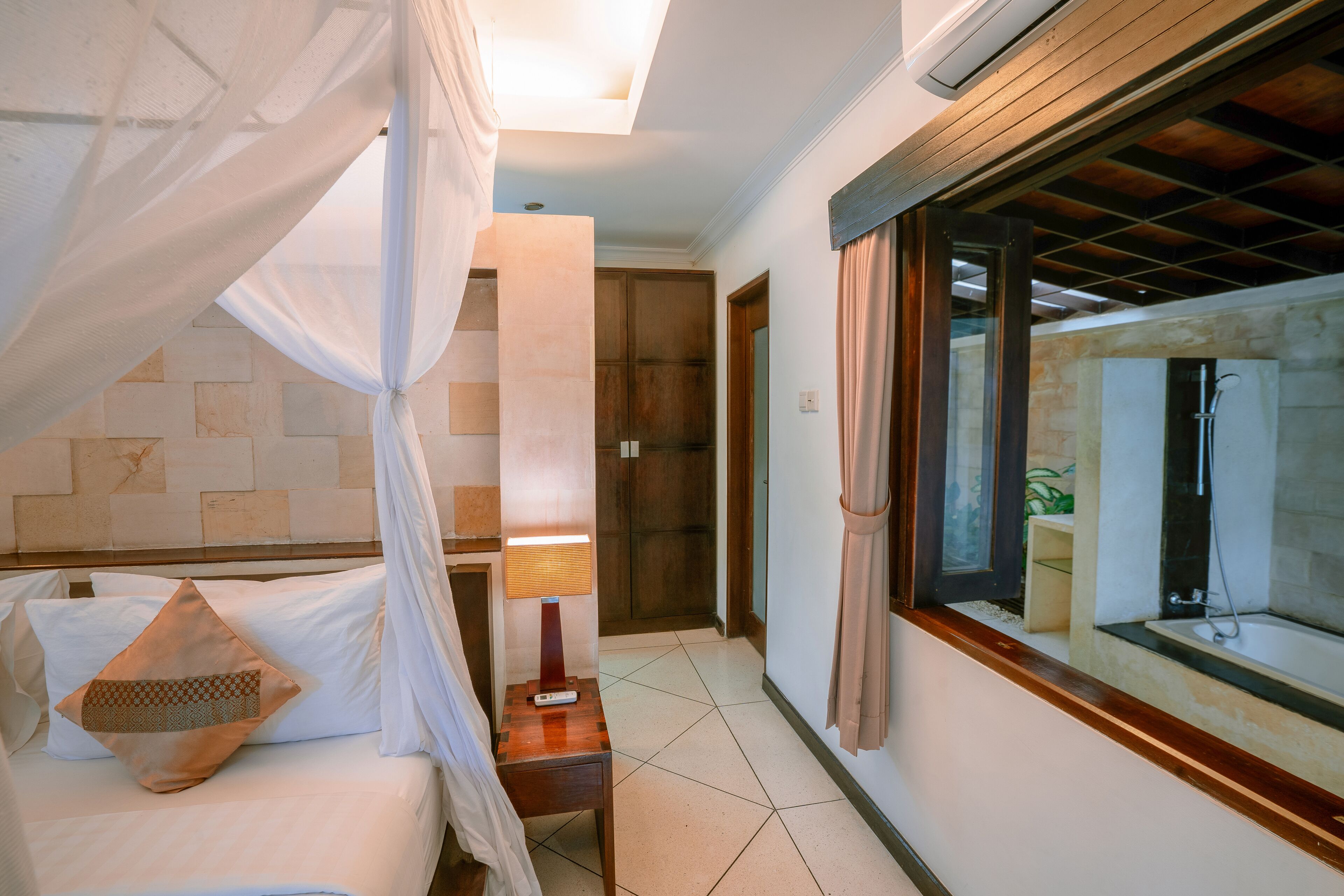A bedroom with a bed, a nightstand, a lamp, and a window with curtains.