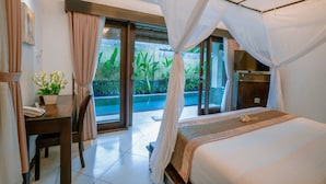 A hotel room with a bed, a desk, a chair, a potted plant, and a view of greenery outside. - The Maya Seminyak Villas (Seminyak)