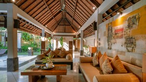 A spacious lobby with a high ceiling, a central seating area with sofas and a coffee table, and a large wall with artwork. - The Maya Seminyak Villas (Seminyak)