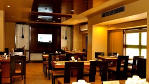 A restaurant with multiple tables and chairs, a television screen, and a ceiling with recessed lighting. - juSTa Hyderabad (Hyderabad)