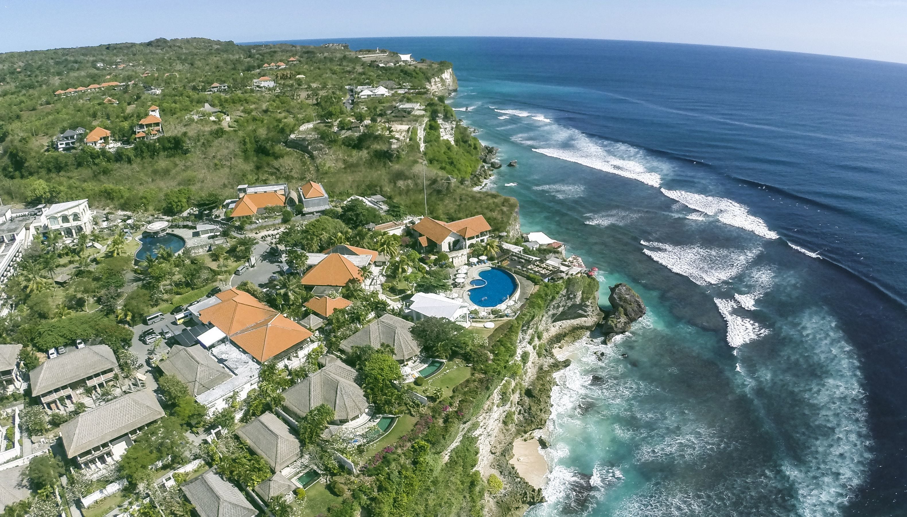 An aerial view of a coastal resort with multiple buildings, a large swimming pool, and ocean views.