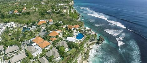 An aerial view of a coastal resort with multiple buildings, a large swimming pool, and ocean views.