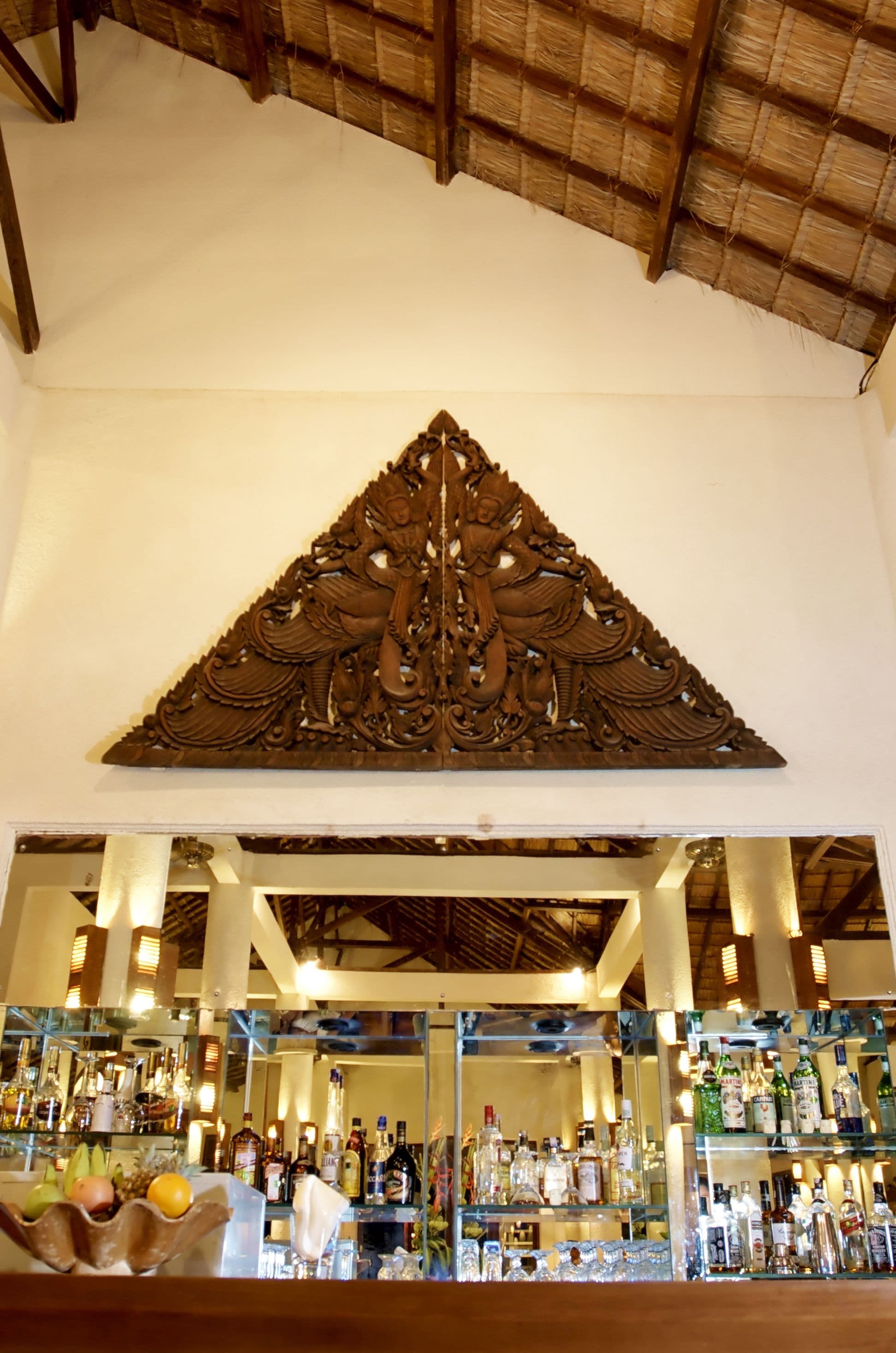 A bar area with shelves of bottles and a decorative wooden carving above.