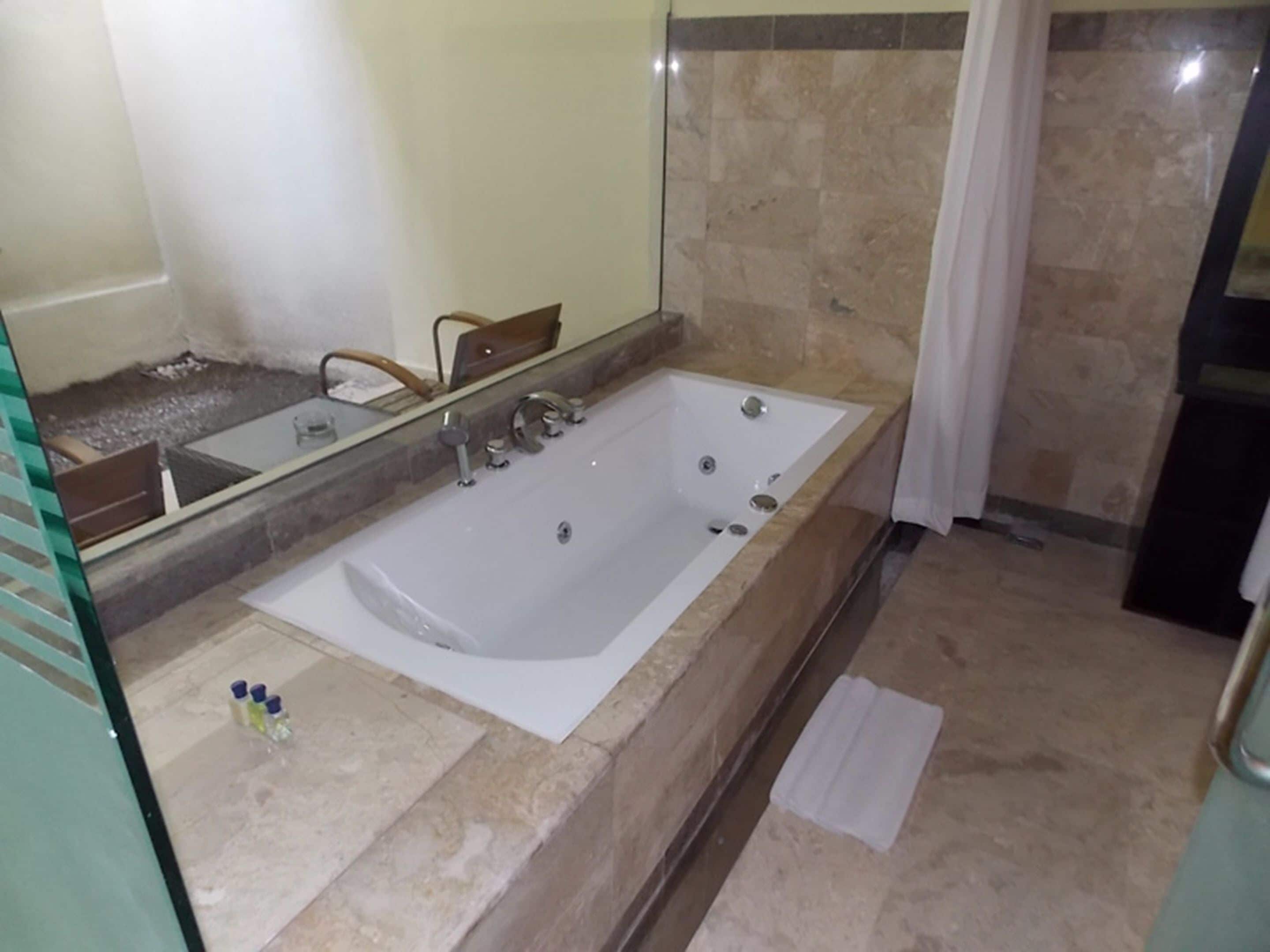 A bathroom with a large bathtub, a mirror, and a shower area.