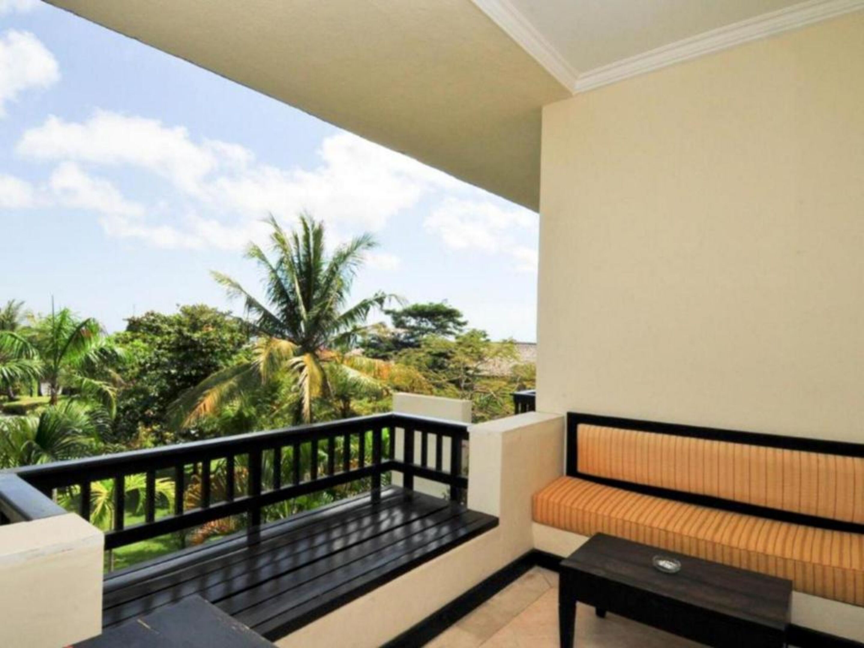 A balcony with a black railing, a beige wall, and a cushioned bench.