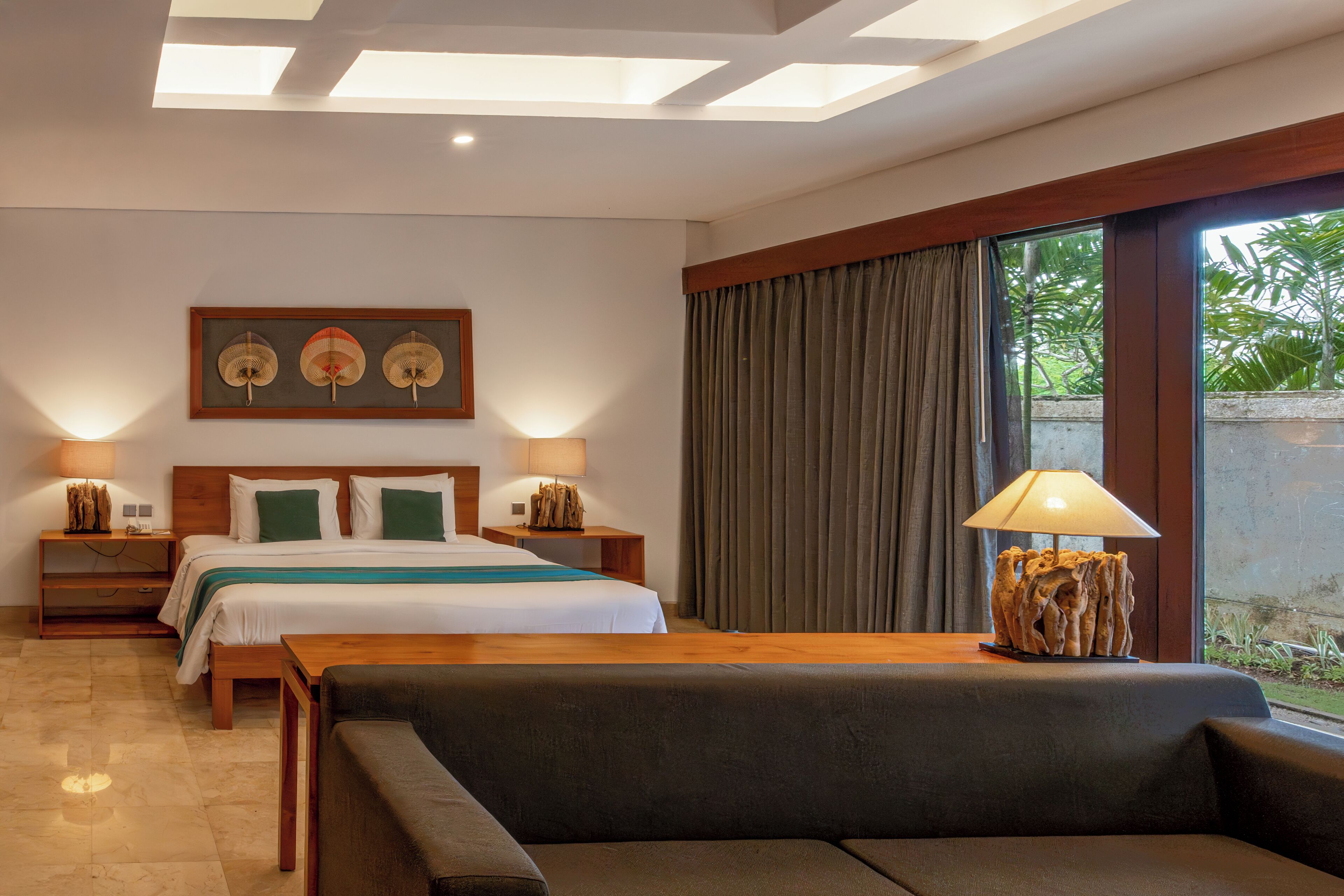 A hotel room with a bed, bedside tables, a sofa, a lamp, and a window with curtains.